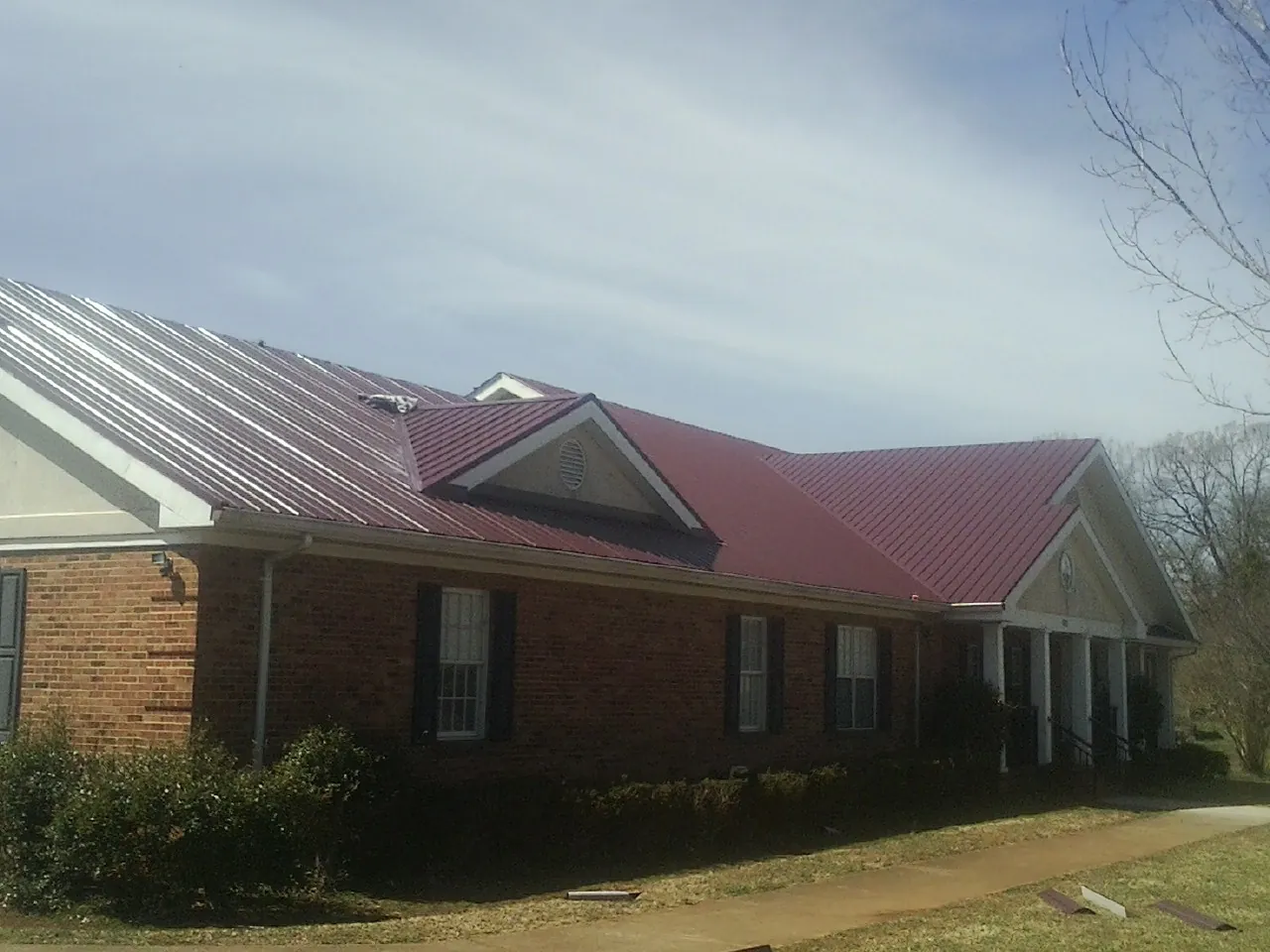 Red metal roof with gabled entries on a long brick building, from a Hail Damage Roof Repair job in Poughkeepsie