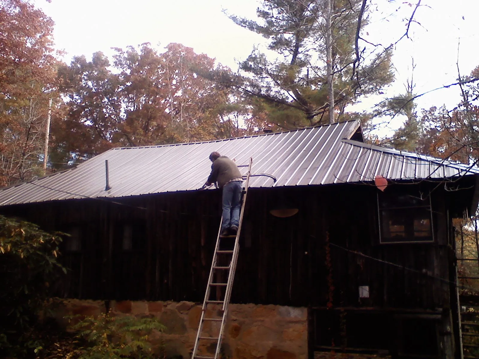 Roofer on a ladder working along the edge of a cabin metal roof in Poughkeepsie
