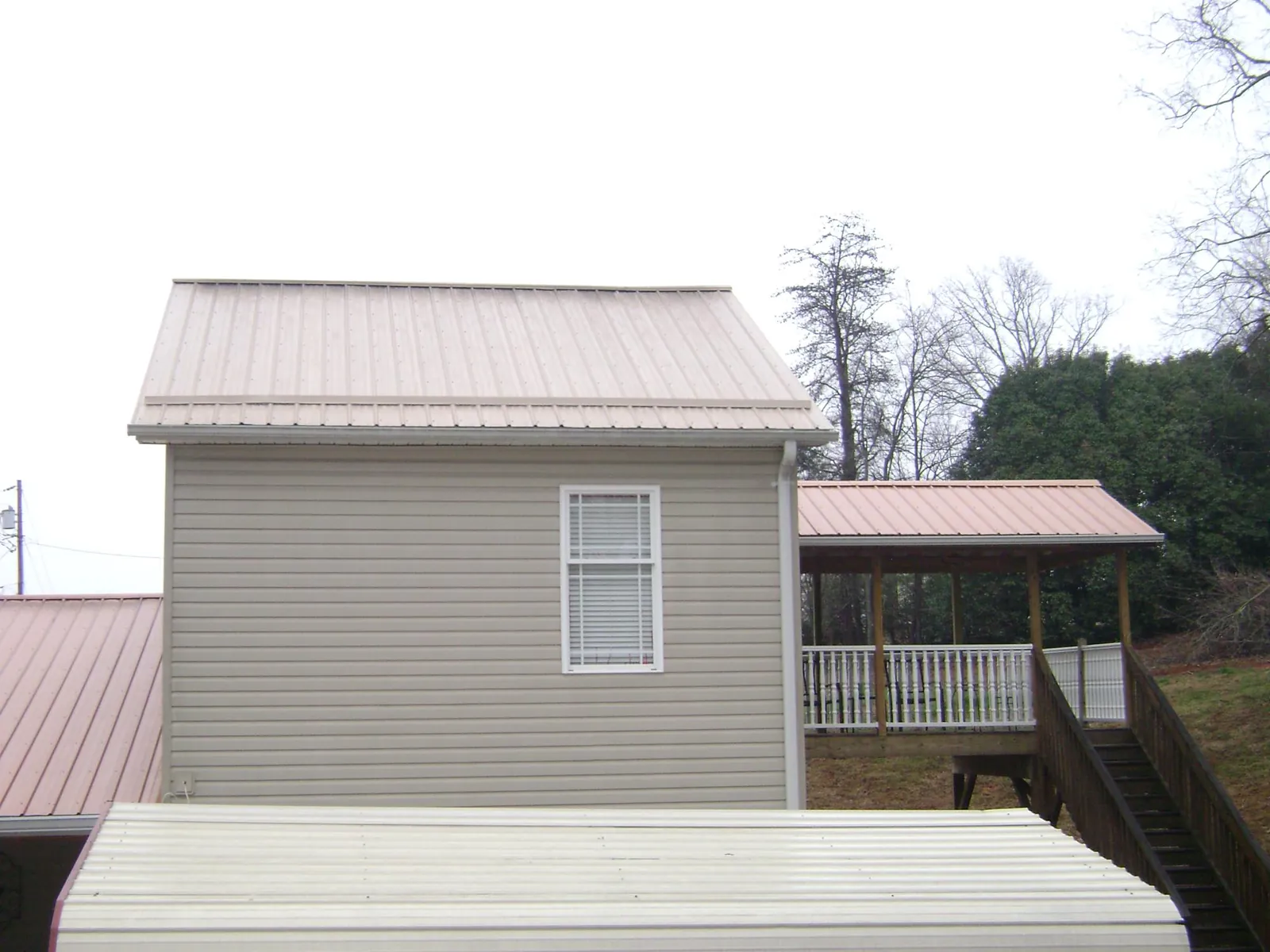 Tan metal roofs on a two story addition and attached porch, from a Roof Replacement job in Poughkeepsie
